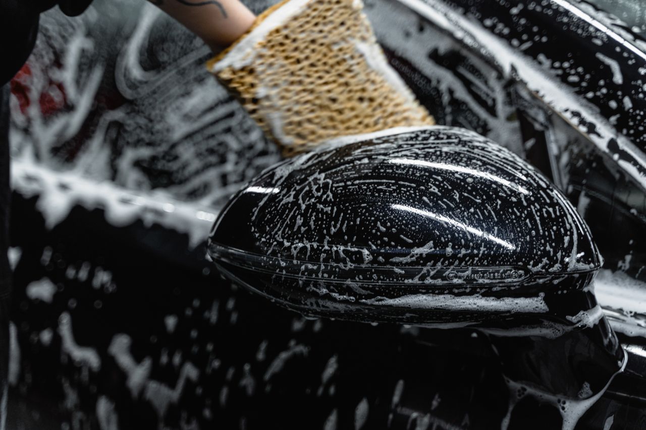 creative-approach-img Hand scrubbing a car mirror with a sponge covered in soap at a car wash.