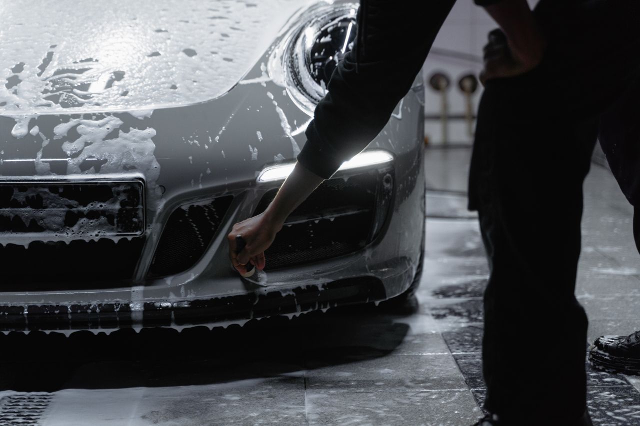 about-img A close-up view of a car being meticulously washed with soap in a garage setting, emphasizing cleanliness and care.